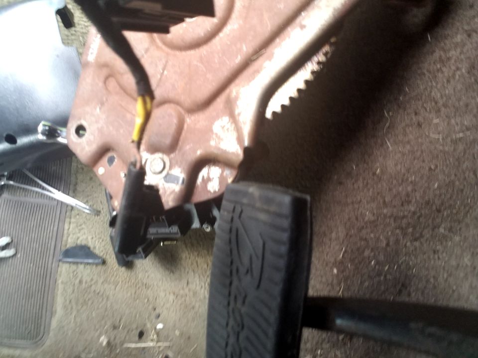 Close-up of a vehicle's brake pedal and rusty metal bracket with wiring
