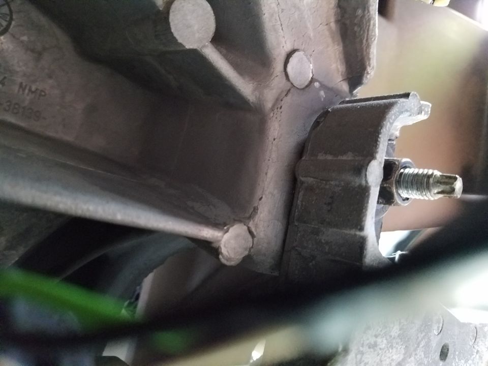 Close-up of a metal bracket with a bolt attached to a larger metal component, with some green material visible below