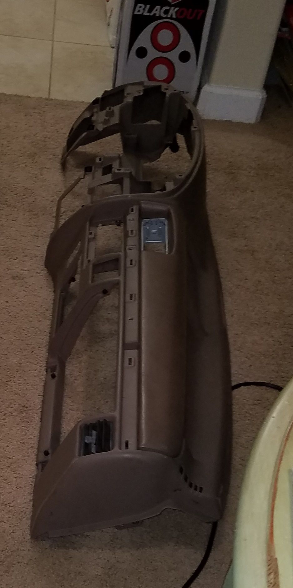 Brown plastic dashboard frame, disassembled, on carpet. A "BLACKOUT" box is visible in the background