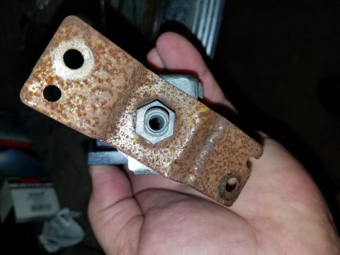 1994 Ford Bronco - A close-up view of a rusted metal bracket with a bolt and nut, held by a hand.