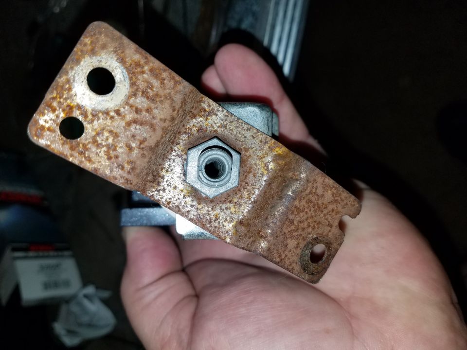 Rusted metal bracket with bolt and nut held in hand