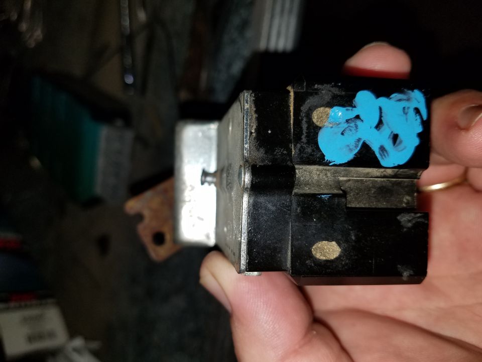 Hand holding a black automotive electrical part with blue paint marks