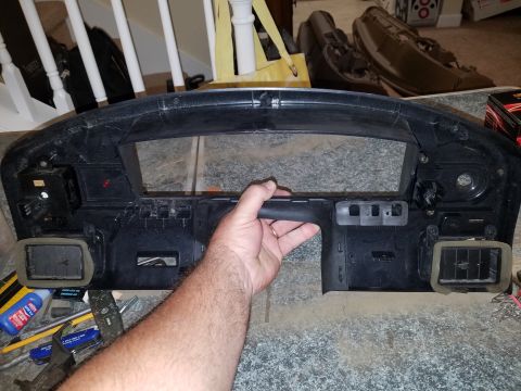 1994 Ford Bronco - A black dashboard trim panel is held by a hand, revealing air vents and internal mounting structures.