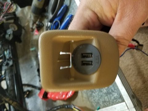 1994 Ford Bronco - Photograph of a hand-held dual-USB power outlet in a tan trim bezel, not a diagram.