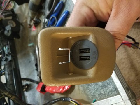 1994 Ford Bronco - Photograph of a hand-held dual-USB charger in a tan trim bezel, not a document.