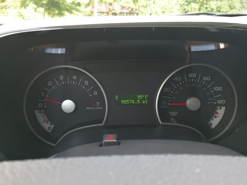 Vehicle instrument cluster with tachometer, speedometer, fuel gauge, and digital display showing temperature and mileage.