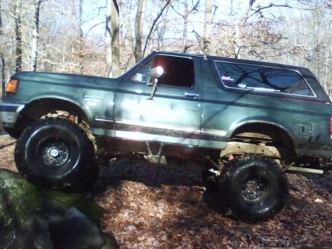 1989 Ford Bronco - This lifted Ford Bronco navigates a wooded area with large off-road tires.