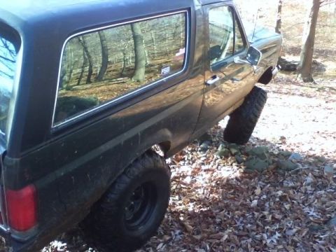 1989 Ford Bronco - 1989 Ford Bronco with off-road tires parked in a wooded area.
