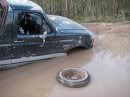 1989 Ford Bronco - Truck submerged in mud with its front passenger wheel detached.