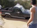 1989 Ford Bronco - Ford pickup truck is stuck in deep mud, with people around it.