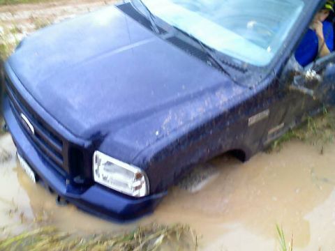 1989 Ford Bronco - This blue pickup truck is deeply stuck in a muddy area, with its front end submerged.