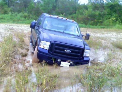 1989 Ford Bronco - A blue Ford truck is stuck in muddy terrain, with its front end partially submerged.