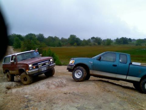 1989 Ford Bronco - Two trucks are navigating a challenging off-road course under an overcast sky.