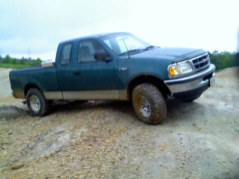 1989 Ford Bronco - This green Ford F-150 pickup truck is shown from a three-quarter front angle on a dirt terrain.