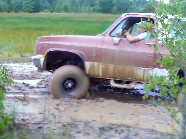 Side view of a red pickup truck stuck in mud, with a driver visible