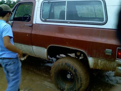 1989 Ford Bronco - A person stands next to a muddy off-road SUV in a wet, outdoor environment.