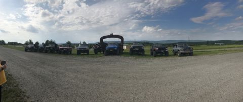 1989 Ford Bronco - A group of off-road vehicles are lined up on a dirt road under a cloudy sky.