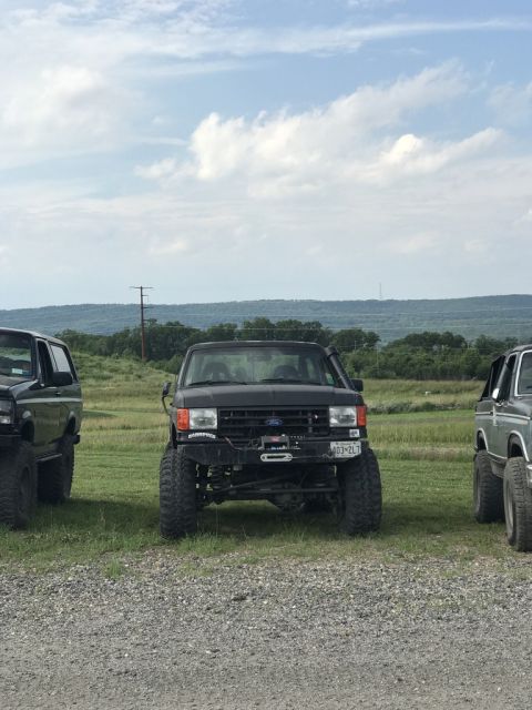 1989 Ford Bronco - Three lifted off-road vehicles are parked in a field under a cloudy sky.