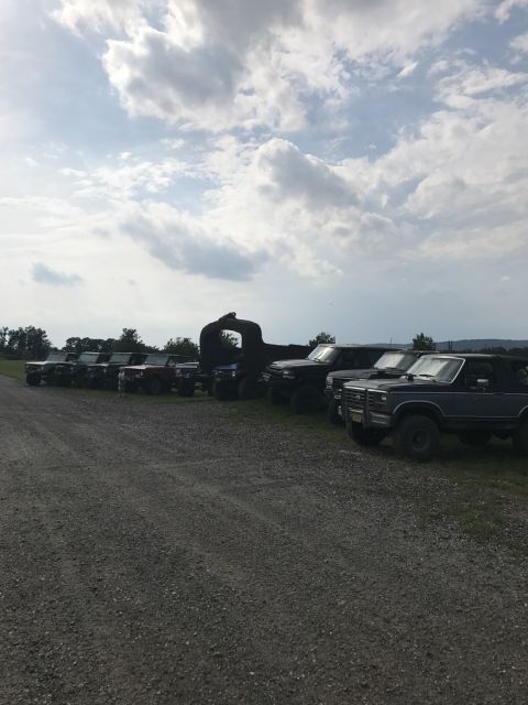 1989 Ford Bronco - Several SUVs and trucks are parked in a line on a gravel lot under a cloudy sky.
