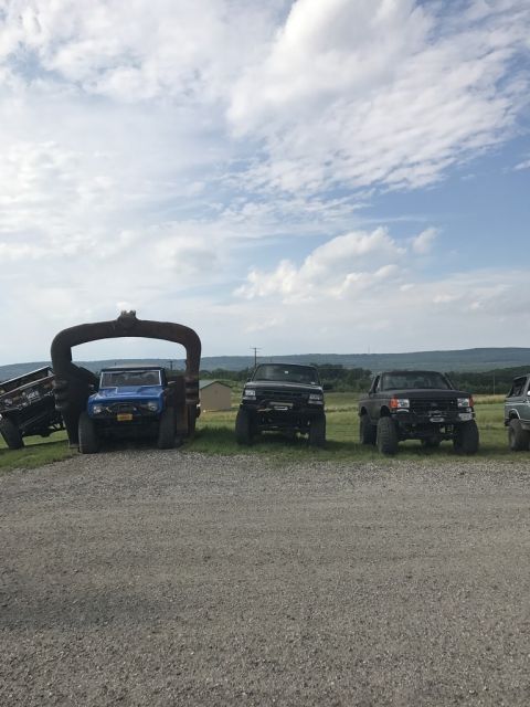 1989 Ford Bronco - Several lifted trucks and a blue SUV are parked in a gravel lot under a cloudy sky.