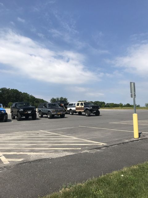 1989 Ford Bronco - Several SUVs and trucks, including a gray 1987 Ford Bronco, are parked in an outdoor lot under a partly cloudy sky.