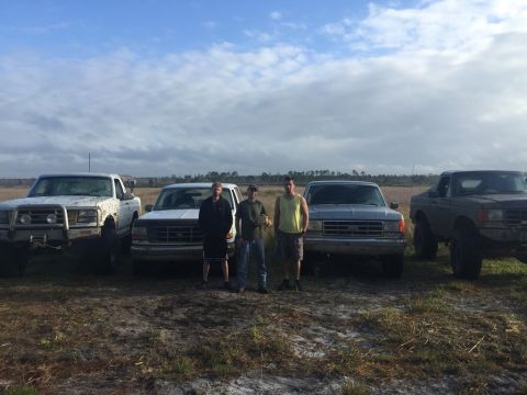 1989 Ford Bronco - Three men pose with four pickup trucks in an open field under a cloudy sky.