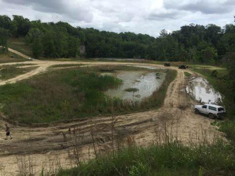 1989 Ford Bronco - Several vehicles navigate a challenging off-road course with muddy tracks and a body of water.