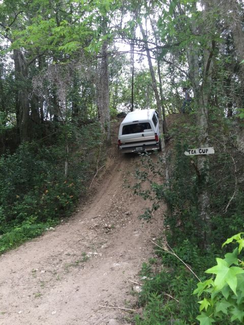 1989 Ford Bronco - White 1989 Ford Bronco navigates a challenging dirt incline surrounded by trees.