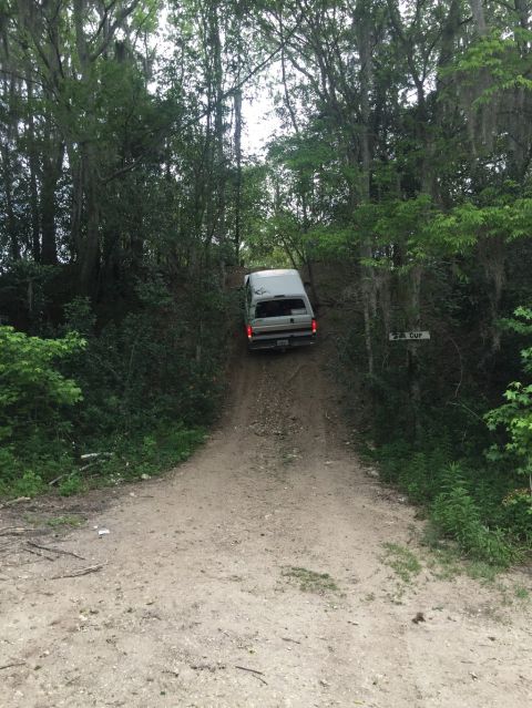 1989 Ford Bronco - A white van navigates a steep dirt path surrounded by dense trees and foliage.