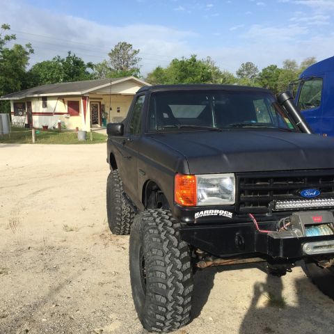 1989 Ford Bronco - A modified black Ford Bronco sits parked on a dirt lot, showing off its off-road capabilities.