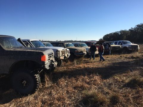 1989 Ford Bronco - A group of trucks are parked in a grassy field under a clear blue sky.