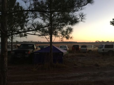 1989 Ford Bronco - Several SUVs and trucks, including a 1989 Ford Bronco, are parked in a field during a sunrise event.