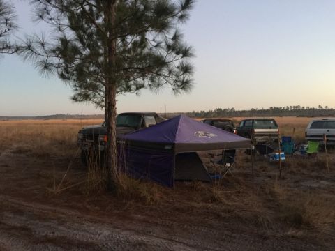1989 Ford Bronco - Multiple SUVs are parked at a campsite with a tent and chairs set up in a grassy field.