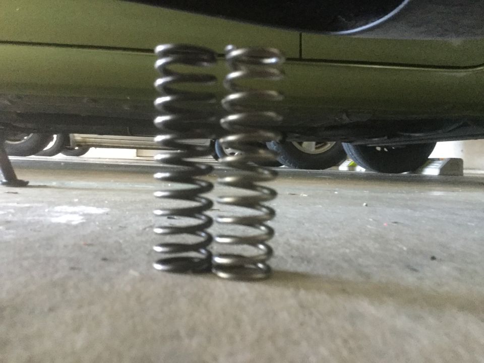 Two metal suspension springs on a concrete floor, with the underside of a green vehicle visible above