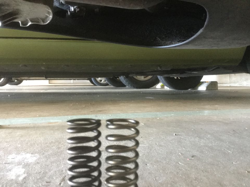 Two suspension springs in foreground, underside of a green vehicle and wheels in background