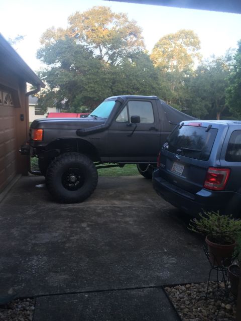 1989 Ford Bronco - A modified black Ford Bronco is parked beside a blue SUV in a driveway.