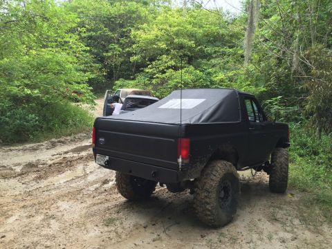 1989 Ford Bronco - A black 1989 Ford Bronco navigates a muddy off-road trail with other vehicles in the background.