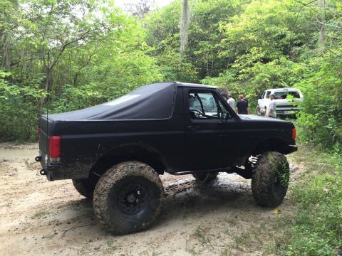 1989 Ford Bronco - Modified 1989 Ford Bronco navigating a muddy off-road trail with a soft top.