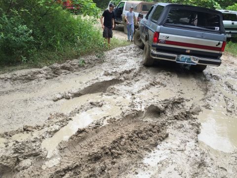 1989 Ford Bronco - Several vehicles navigate a challenging muddy trail, with one Bronco struggling to gain traction.