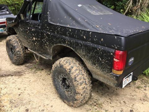 1989 Ford Bronco - This 1989 Ford Bronco is heavily mud-splattered, indicating it has been used for off-roading. Another vehicle is partially visible to the l…