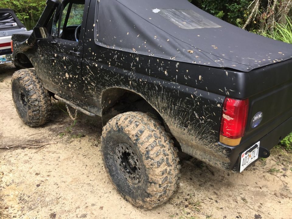 Mud-splattered black 1989 Ford Bronco with large off-road tires, seen from the rear quarter