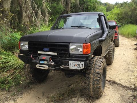 1989 Ford Bronco - Modified black Ford F-150 truck with off-road accessories parked on a dirt path.