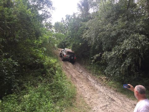 1989 Ford Bronco - A 1989 Ford Bronco navigates a steep, muddy off-road trail surrounded by dense foliage.
