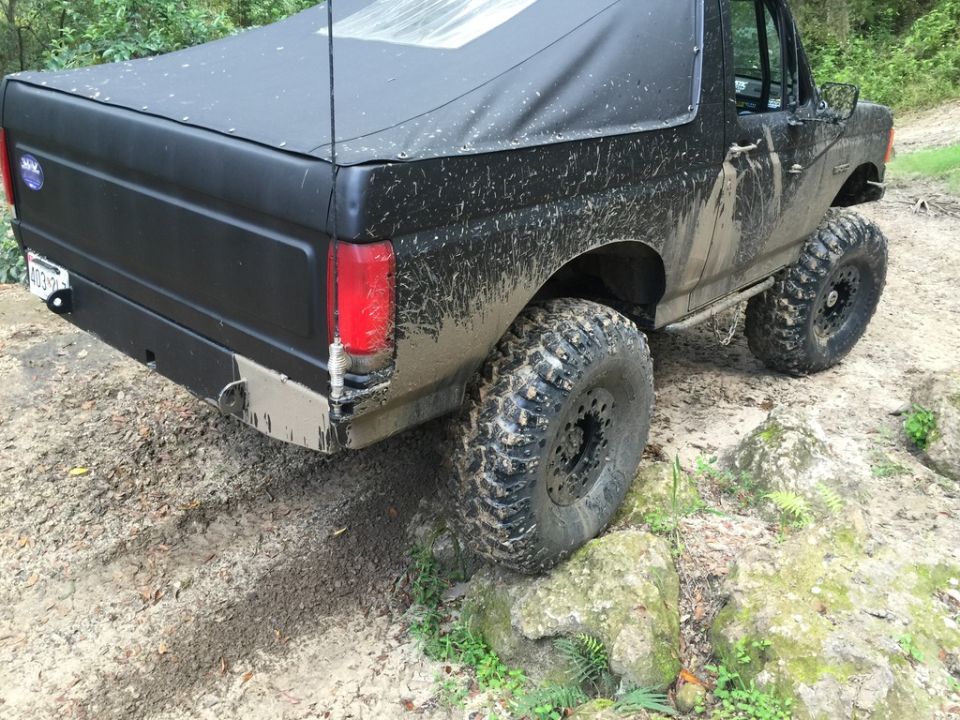 Black 1987 Ford Bronco with a soft top, covered in mud, on a rocky trail