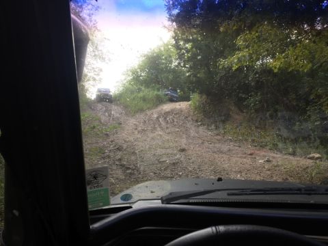 1989 Ford Bronco - Two SUVs navigate a challenging dirt trail, viewed from the perspective of another vehicle on the path.