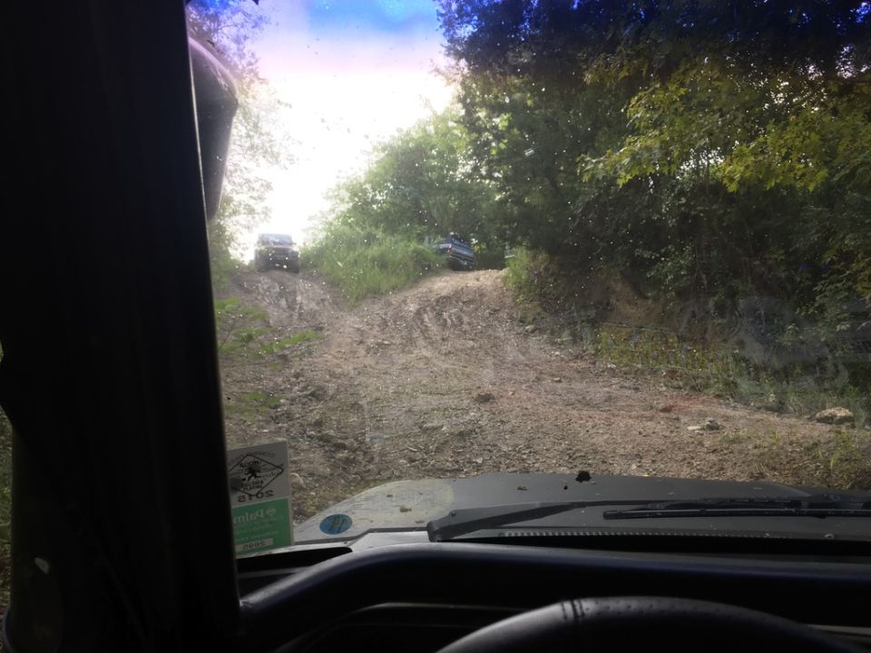 View from inside an SUV looking up a dirt hill at two other SUVs