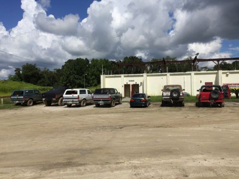 1989 Ford Bronco - Multiple vehicles are parked on a dirt lot under a cloudy sky.