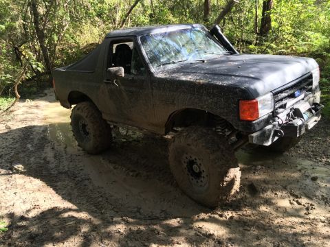 1989 Ford Bronco - This modified Ford Bronco navigates a challenging muddy path, its off-road capabilities.