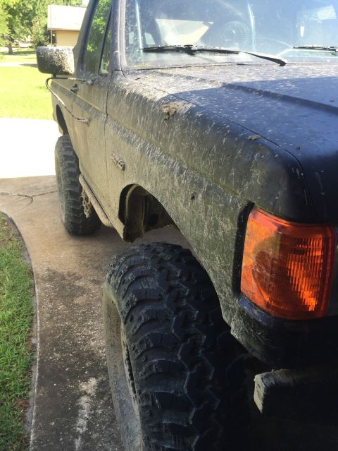 1989 Ford Bronco - A muddy 1987 Ford Bronco is shown from a low angle, highlighting its off-road tires and front end.