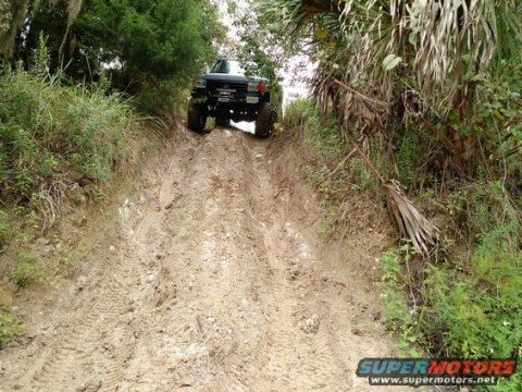 1989 Ford Bronco - A lifted truck navigates a steep, muddy incline surrounded by dense vegetation.